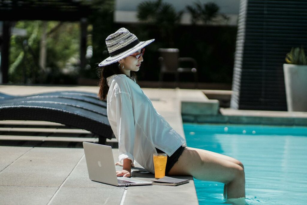 Young ethnic woman resting at poolside after distance work on laptop