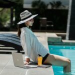 Young ethnic woman resting at poolside after distance work on laptop